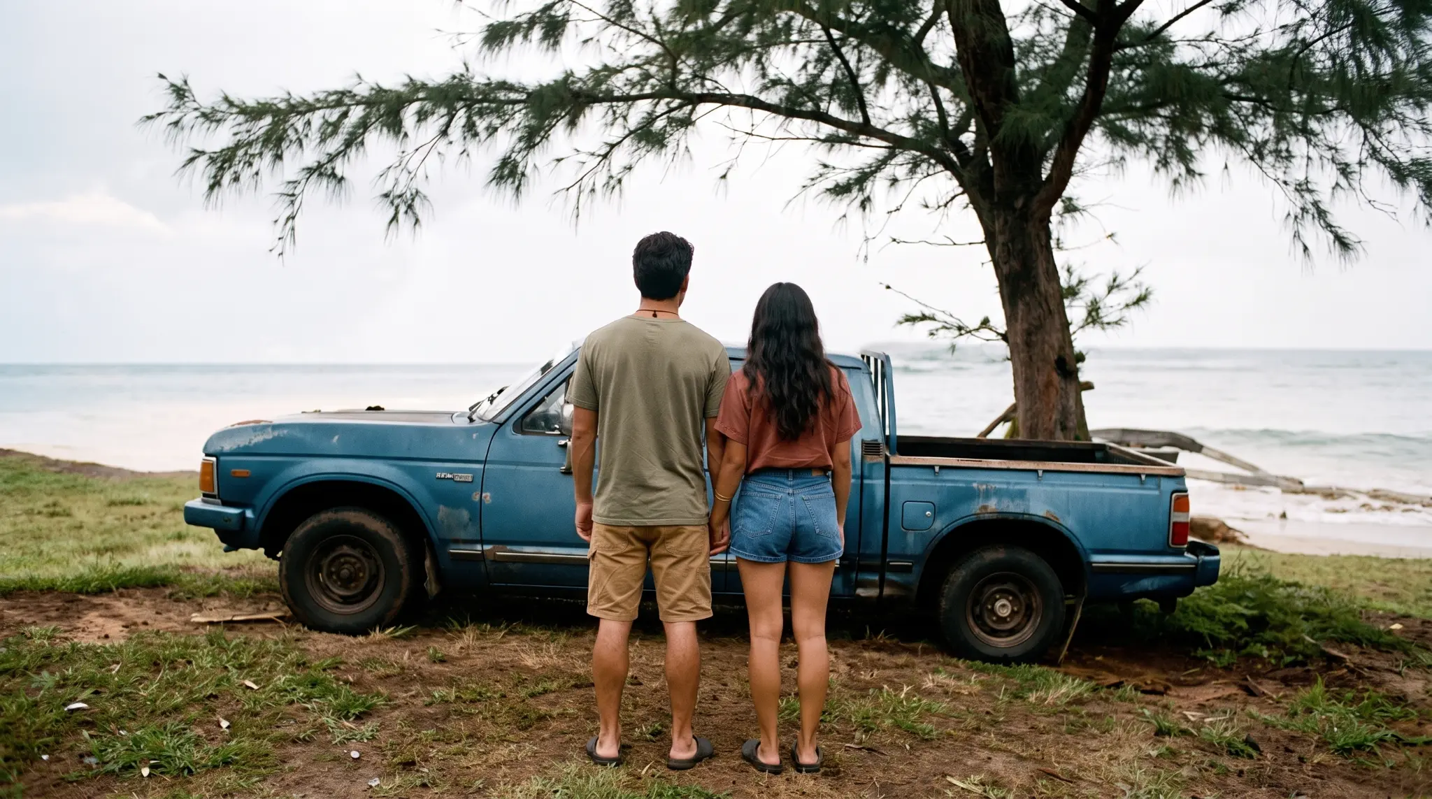 A couple standing beside an old blue truck on the Hawaiʻi coast